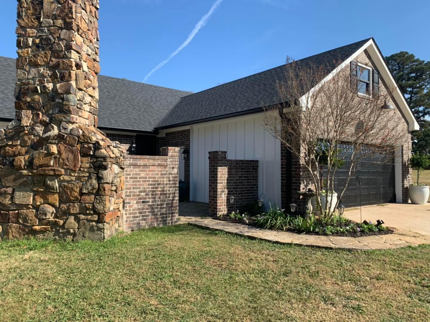 A side view of a house with a stone chimney, a brick wall, white vertical siding, and a dark-roofed garage.