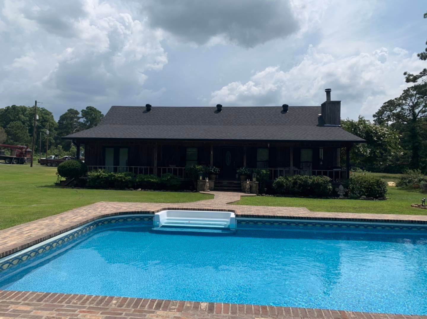 A swimming pool with blue water in the foreground, facing a dark-colored cabin with a dark roof and a porch.