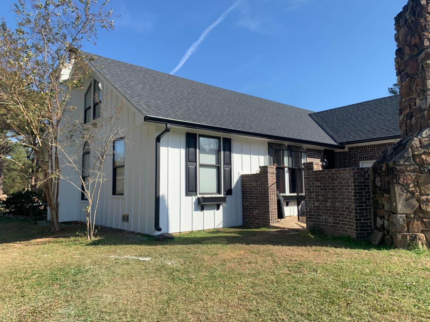 A white board-and-batten house with a dark roof and a prominent stone chimney on a sunny day.