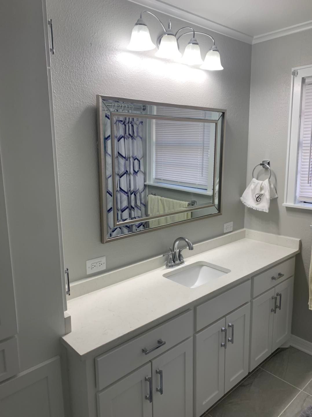 A white bathroom vanity with a chrome faucet, silver-framed mirror, and a modern light fixture against grey walls.