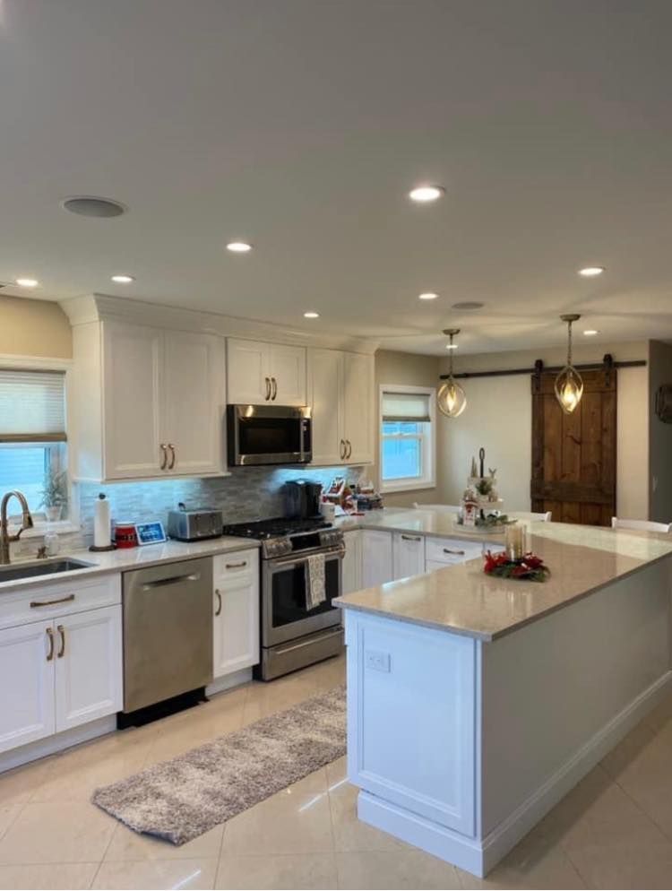 A bright, modern kitchen featuring white cabinets, stainless steel appliances, a center island, and a rustic barn door.
