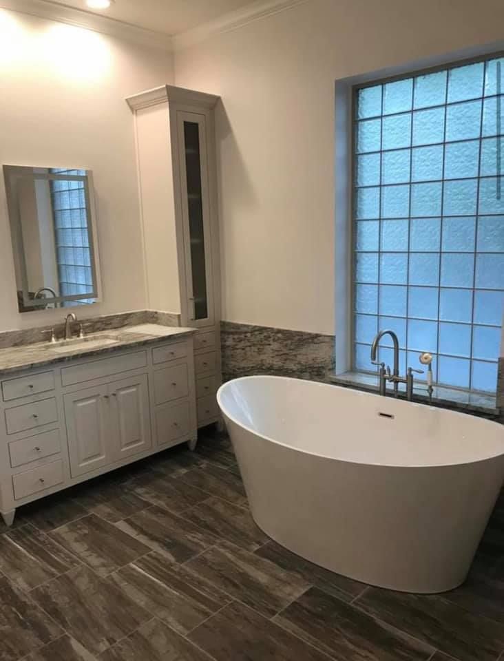 A modern bathroom featuring a white vanity with a tall storage cabinet, a standalone oval tub, and a glass block window.