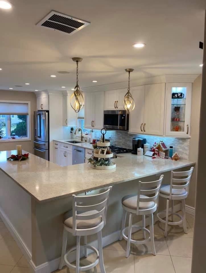 A kitchen features white cabinets, a large island with three white bar stools, and warm pendant lighting.