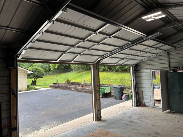Open garage with concrete floor, driveway, and green hillside outside.