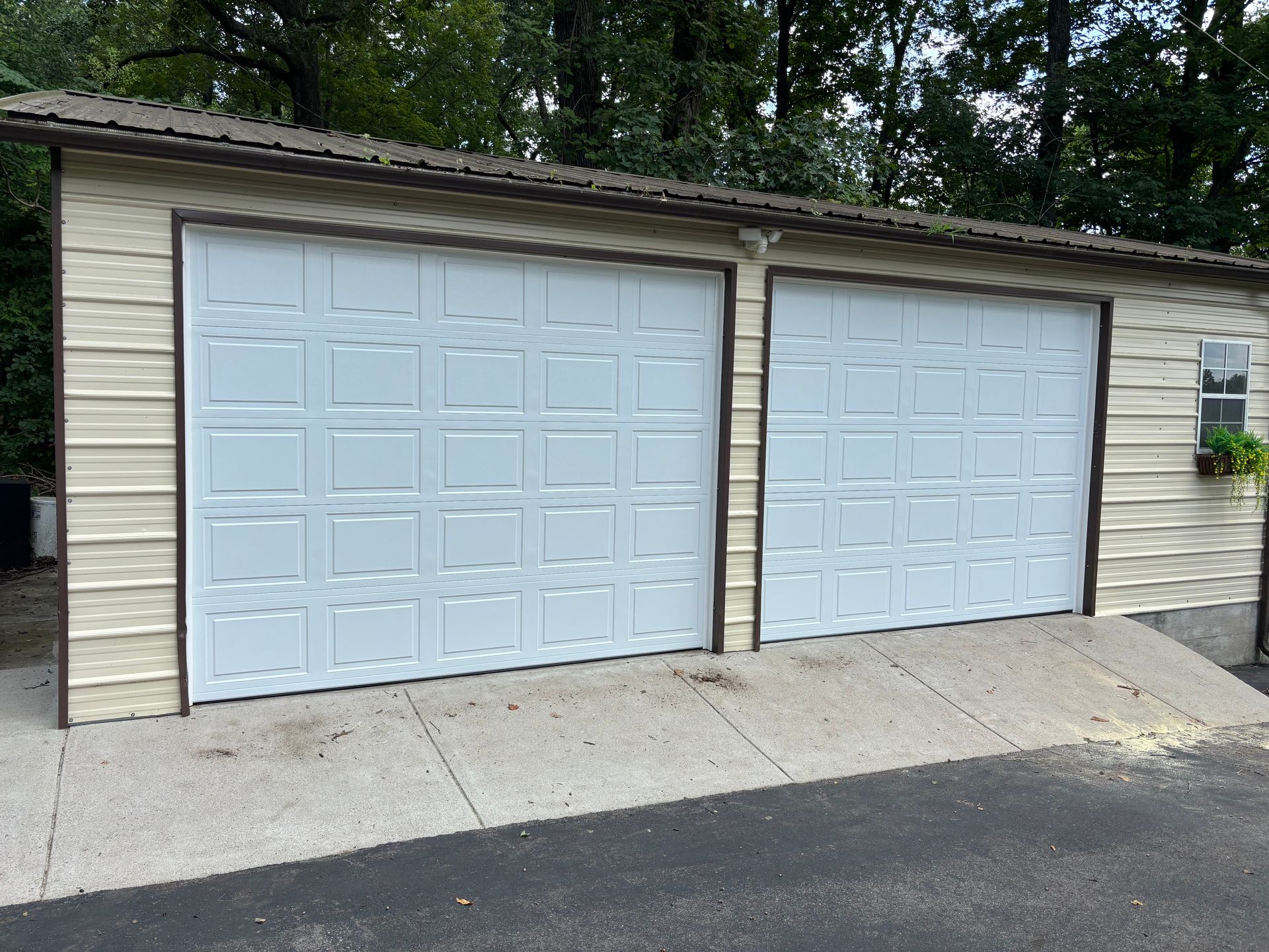 Two white garage doors on a tan house with a concrete driveway and trees behind.