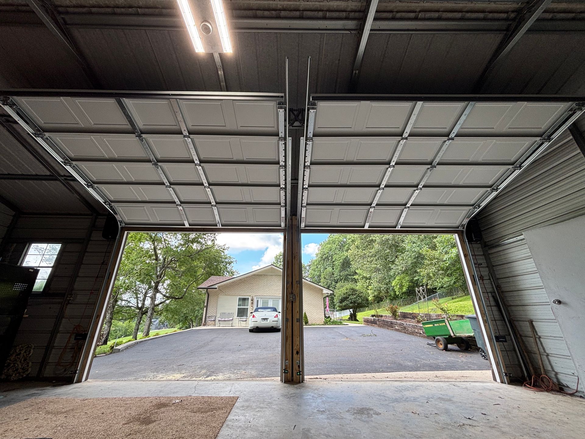 Empty garage interior opening to a gravel driveway, with a house and trees visible outside.