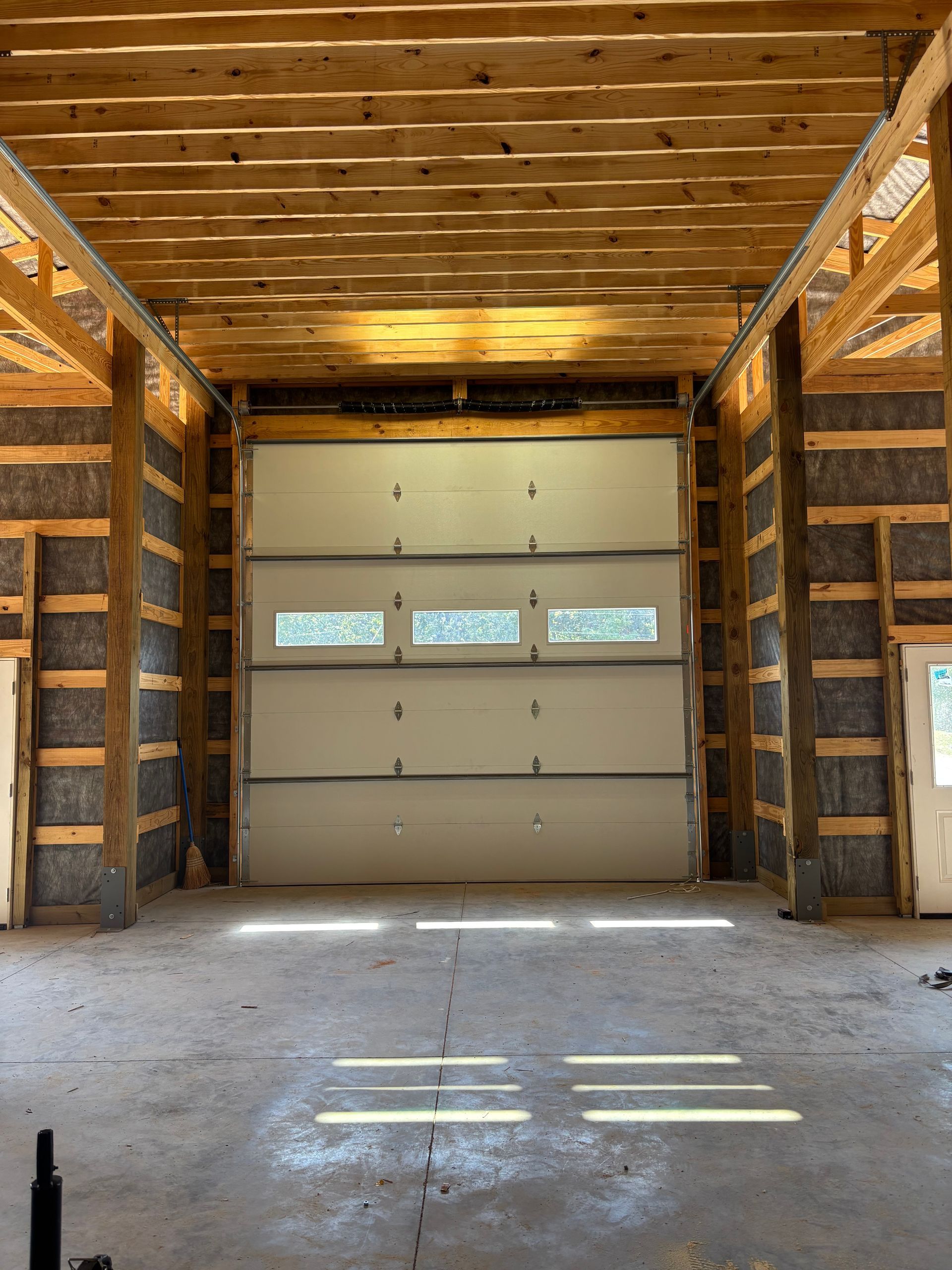 Empty wooden garage with a closed white overhead door and concrete floor.