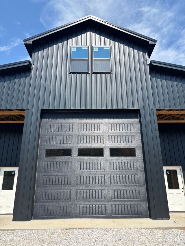 Dark blue barn-style building with a large garage door and two windows on the upper front.