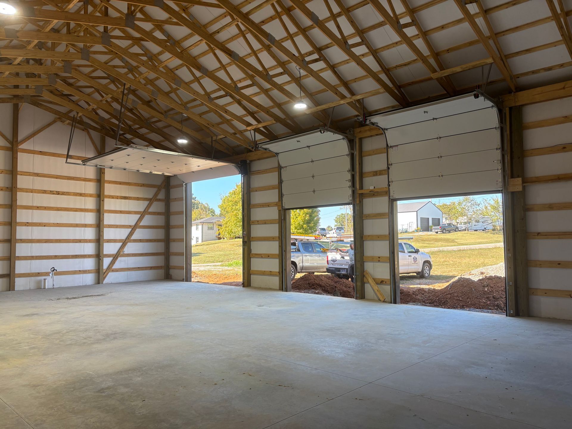 Empty metal warehouse interior with open garage doors and concrete floor, sunlight spilling in