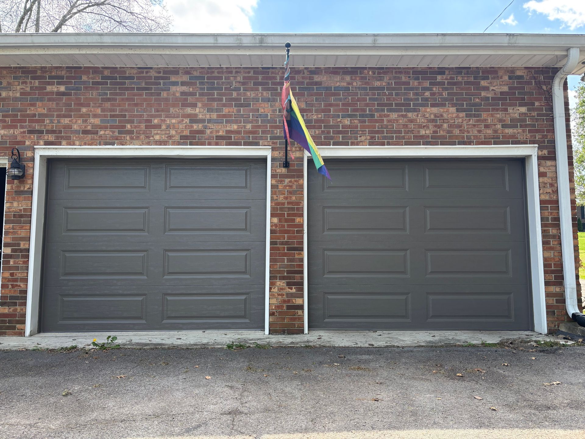 Two gray garage doors on a brick building with a rainbow flag hanging between them
