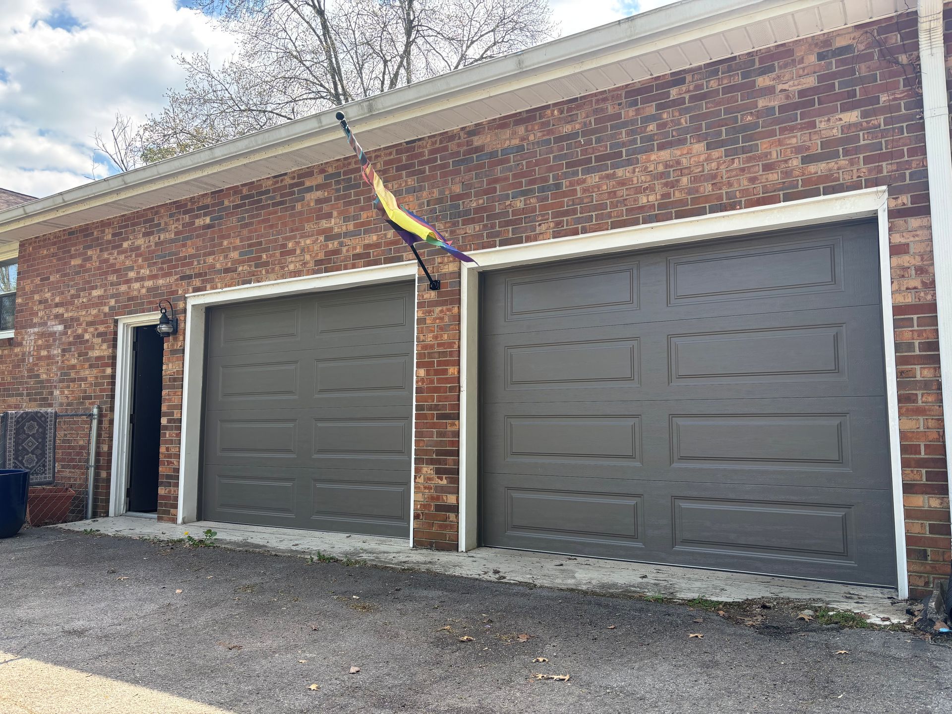 Brick garage exterior with two gray doors and an open side entry under a cloudy sky