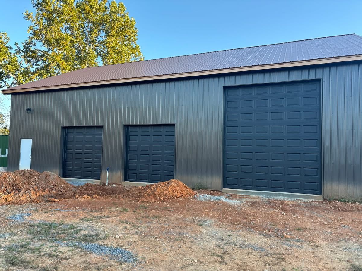 Gray metal barn with three large garage doors, one small door, and piles of dirt in front