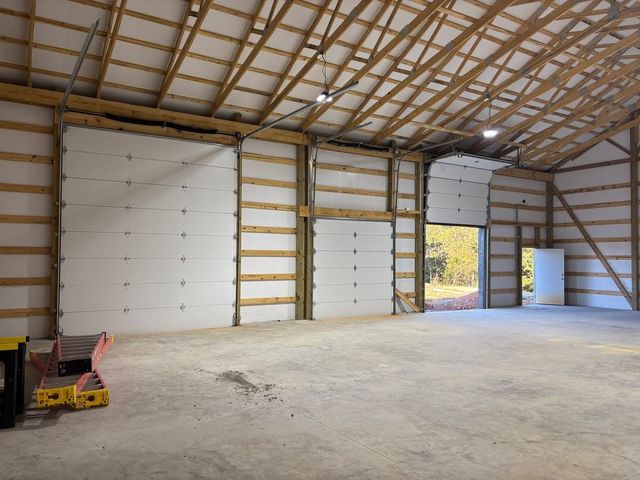 Large unfinished warehouse interior with concrete floor, exposed beams, and two white garage doors.