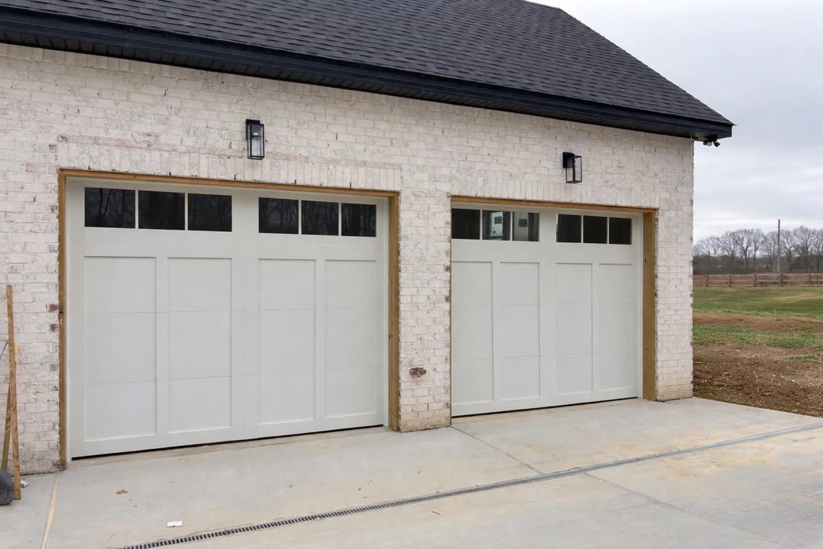 Two white garage doors on a stone house with a dark roof and concrete driveway