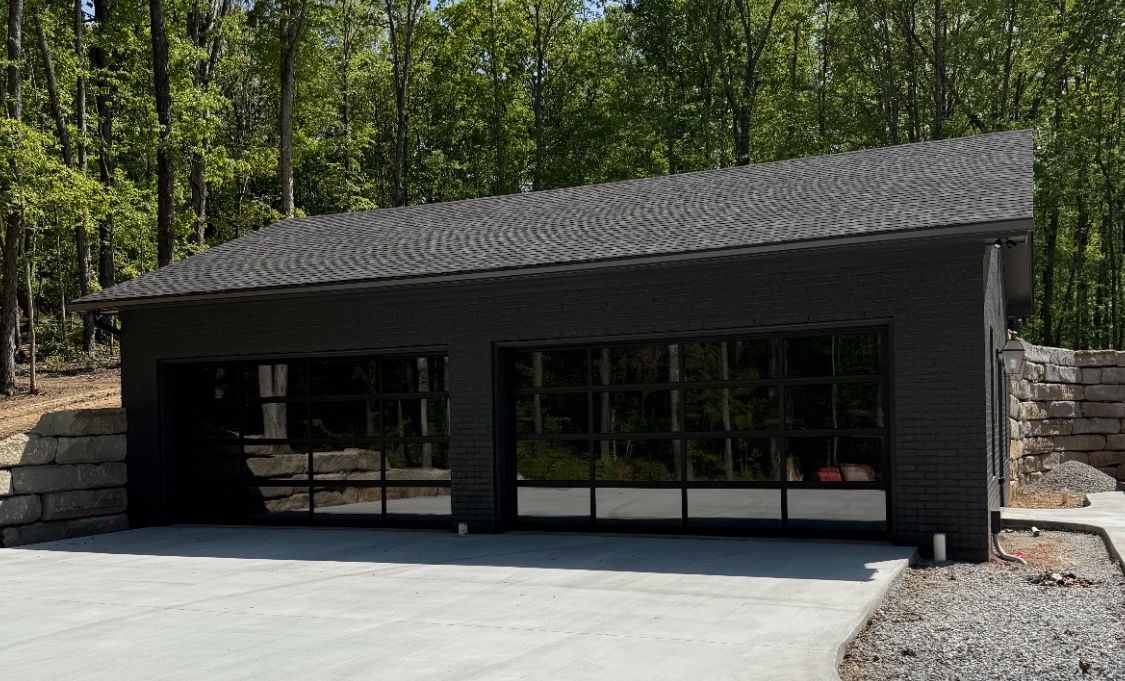 Modern black building with a sloped roof, large windows, and stone accents in a wooded setting