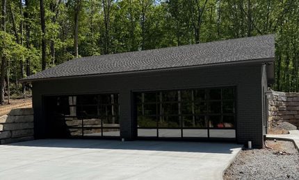 Modern black building with a sloped roof, large windows, and stone accents in a wooded setting