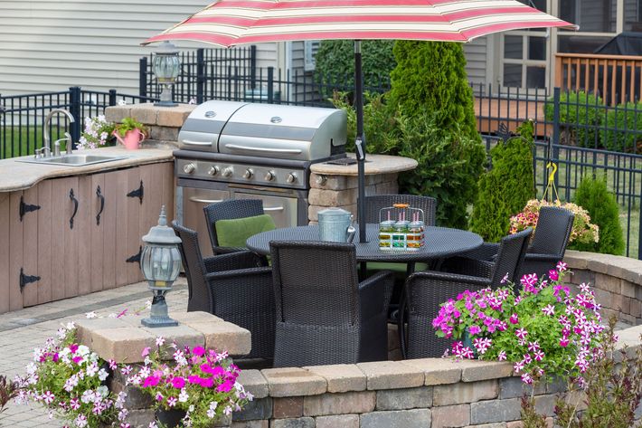 A patio with a table, chairs, umbrella and grill.