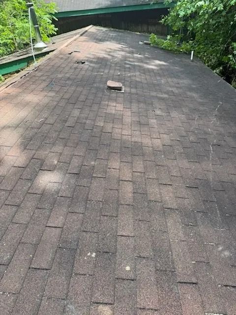 Brown shingle roof with some discoloration and a small brick feature.
