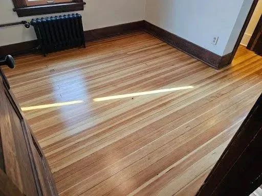Empty room with striped hardwood floor, black radiator, and sunlight streaming across the floor