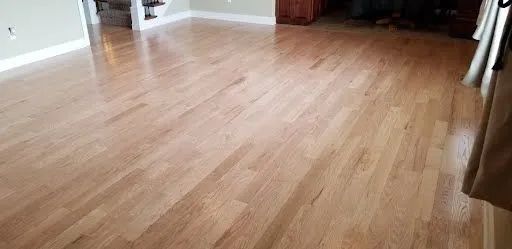 Empty room with light wood flooring and white walls, viewed from a low angle.