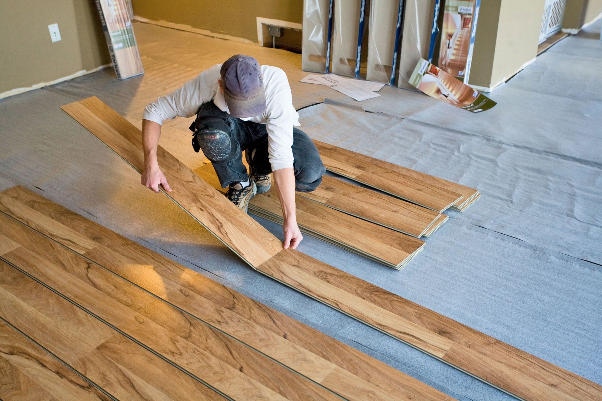 Worker kneeling on a floor, installing wooden planks in a room under construction.