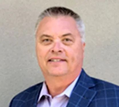 Portrait of a man in a blue checkered blazer and light shirt against a gray background