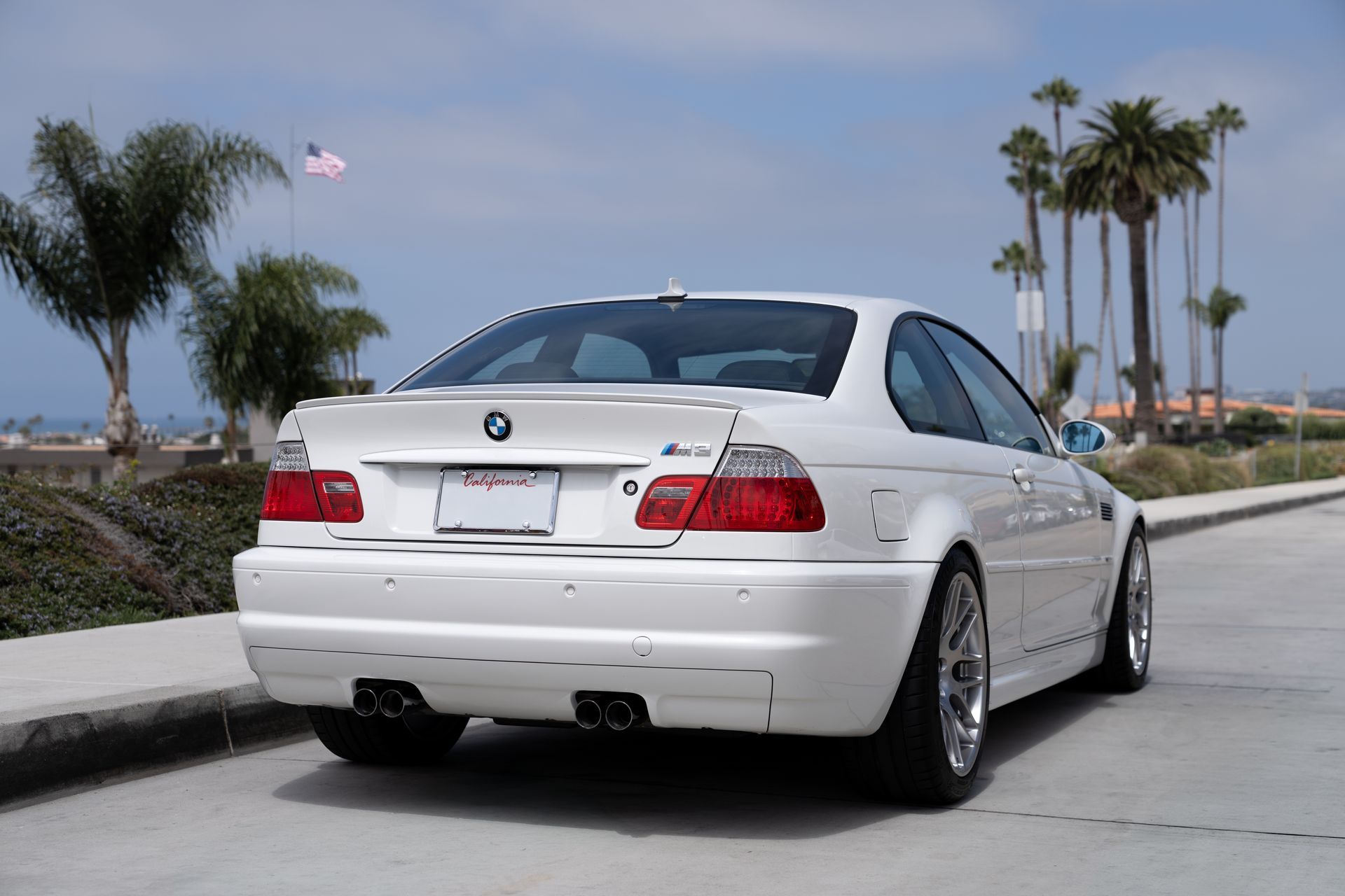 White BMW coupe parked on a sunny street near palm trees and the beach.