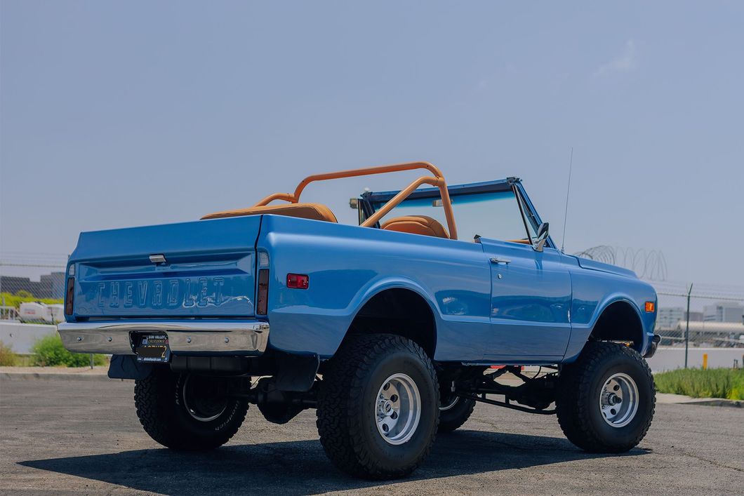 Blue lifted pickup truck with orange roll bars parked outdoors on pavement.