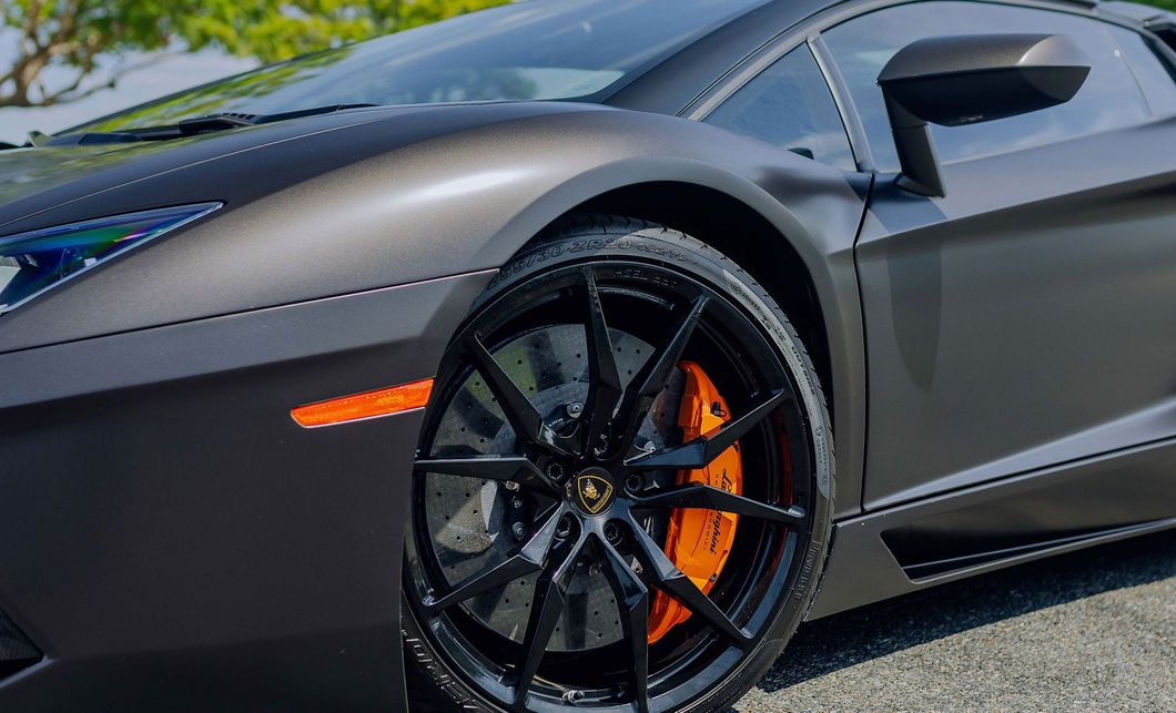 Gray sports car close-up with black rims and orange brake calipers on a sunny road