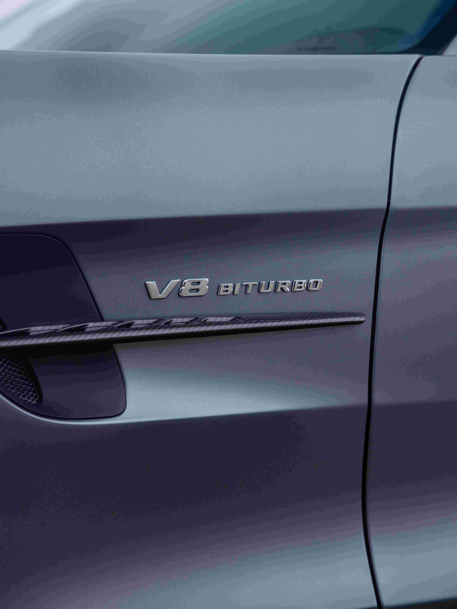 Close-up of a gray car door with V8 Biturbo badge and chrome handle trim.