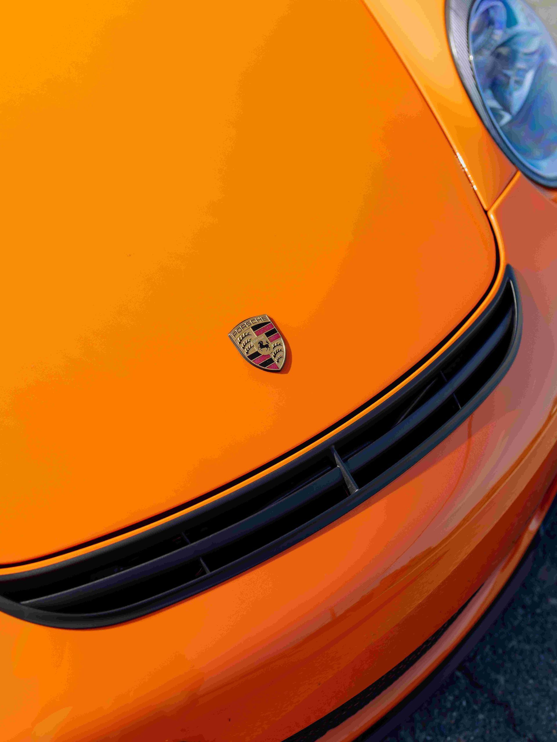 Orange sports car hood with Porsche emblem and headlight