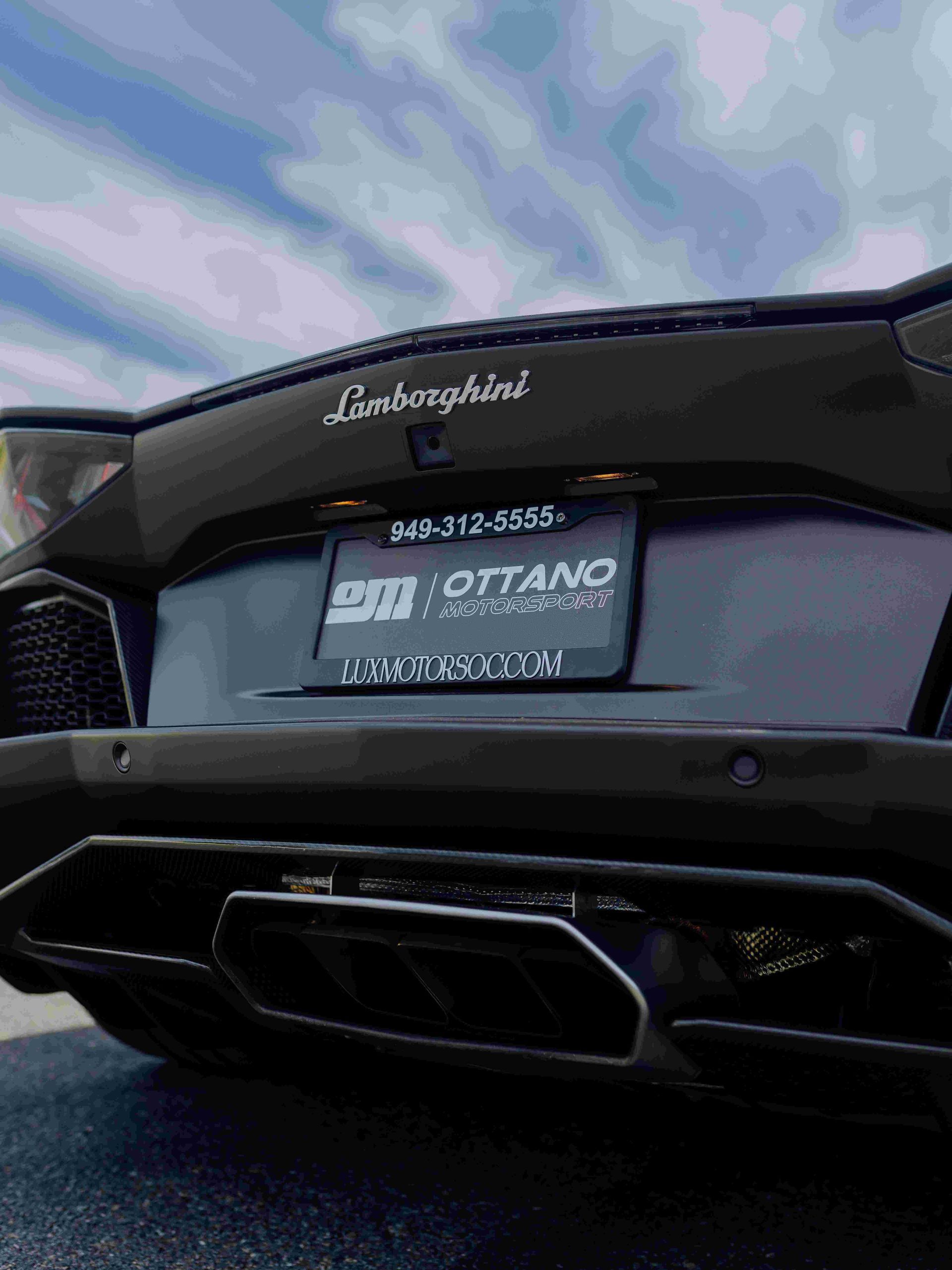 Rear view of a black Lamborghini with a dealer plate against a cloudy sky