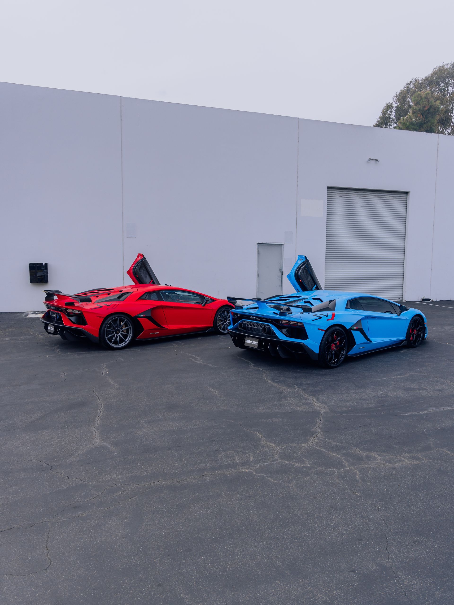 Two sports cars, one red and one blue, parked side by side outside a warehouse.
