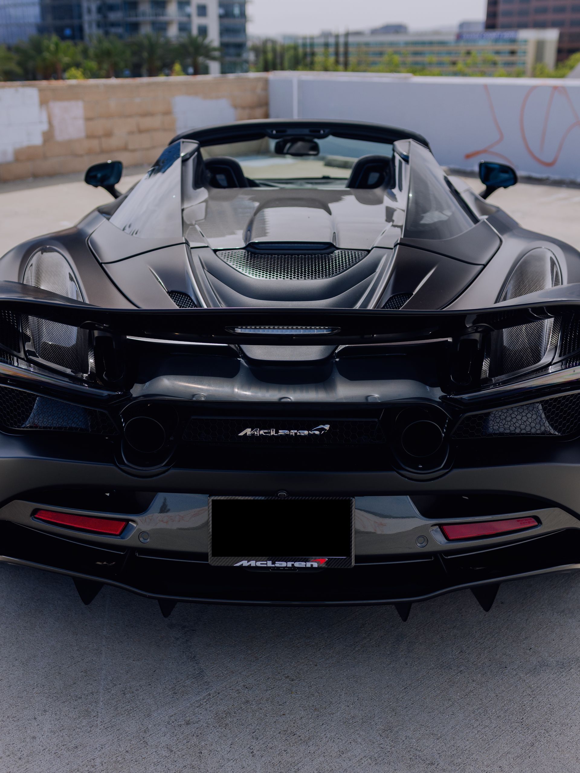 Rear view of a black convertible supercar parked outdoors, showing its rear engine and spoiler.