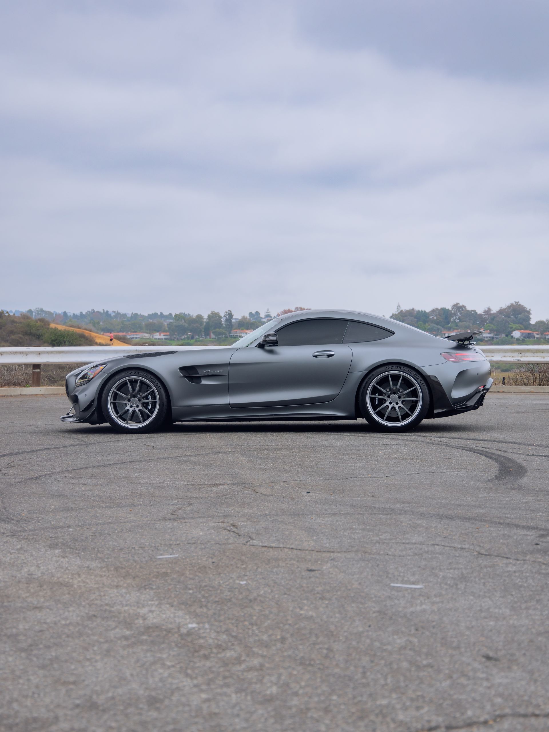 Gray sports car parked on an empty lot under a cloudy sky
