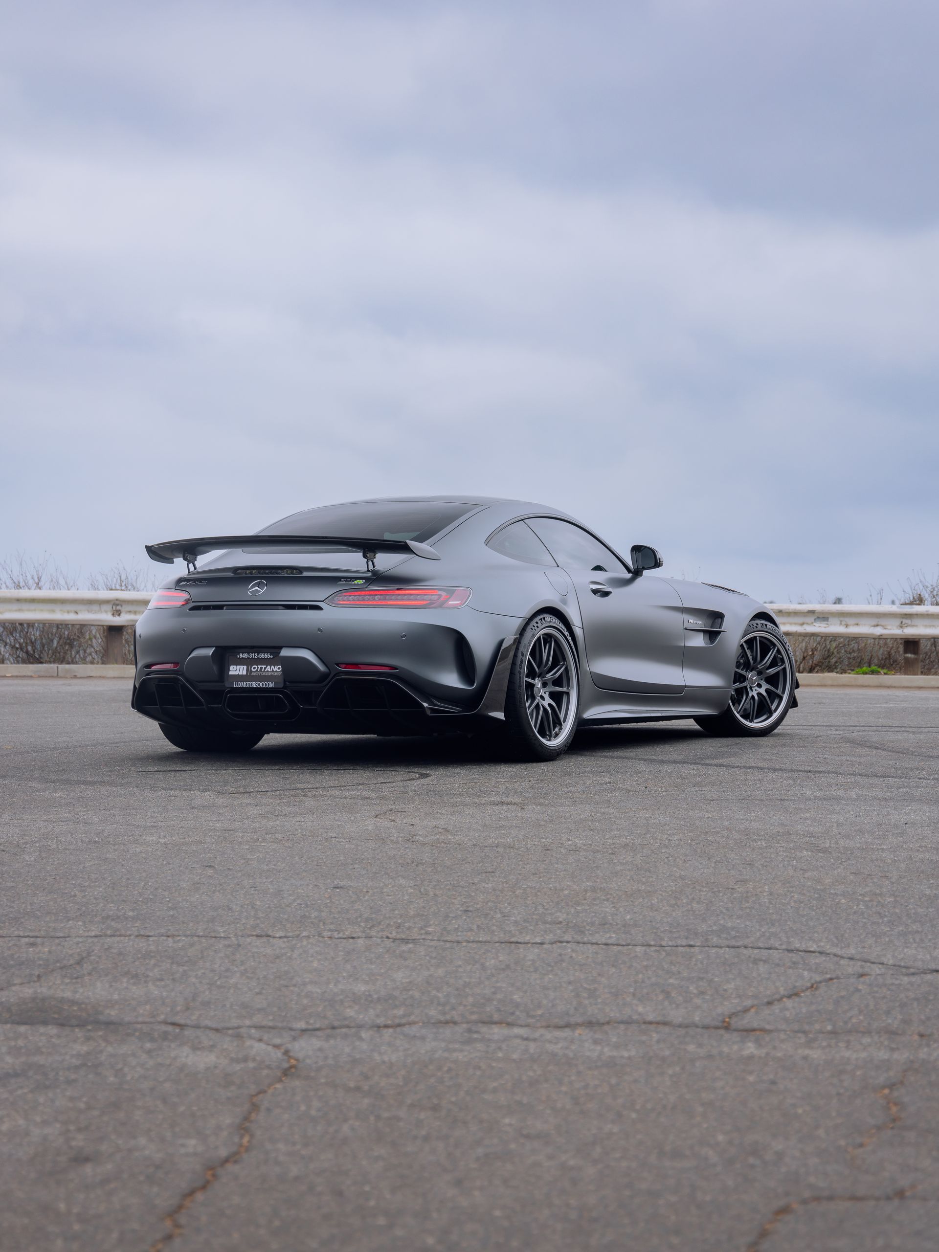 Gray sports car with rear spoiler parked on a road under a cloudy sky