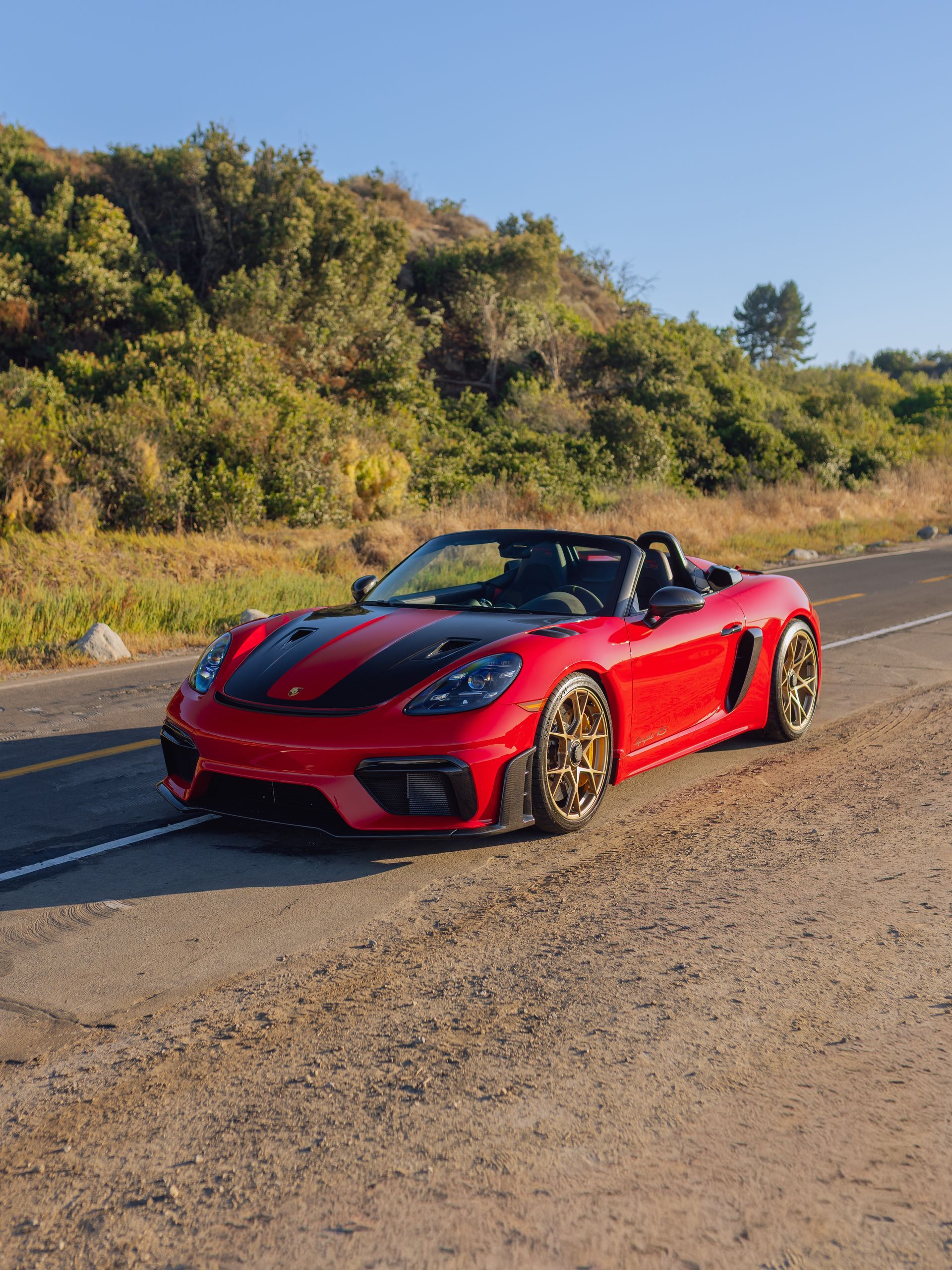 Red sports car parked on a roadside with green hills and clear blue sky in the background