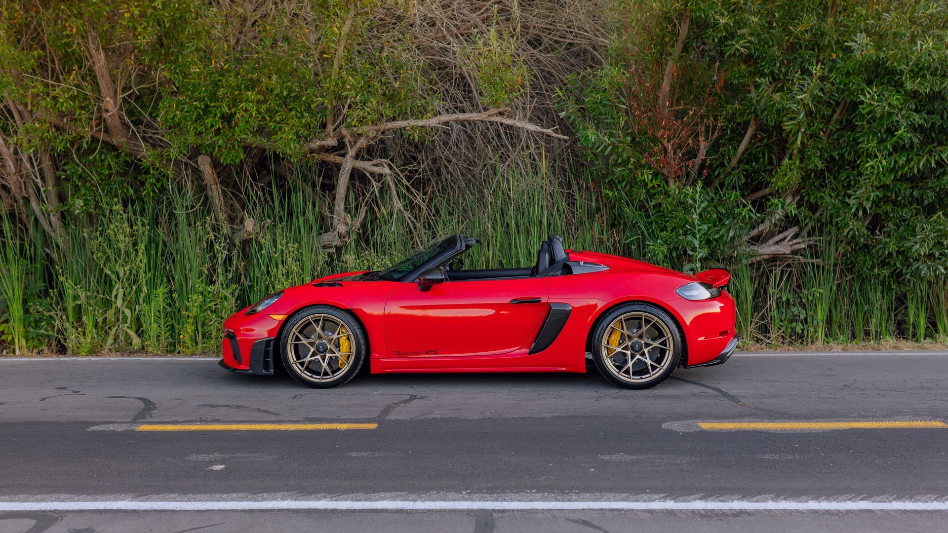 Red convertible sports car parked roadside in front of dense greenery