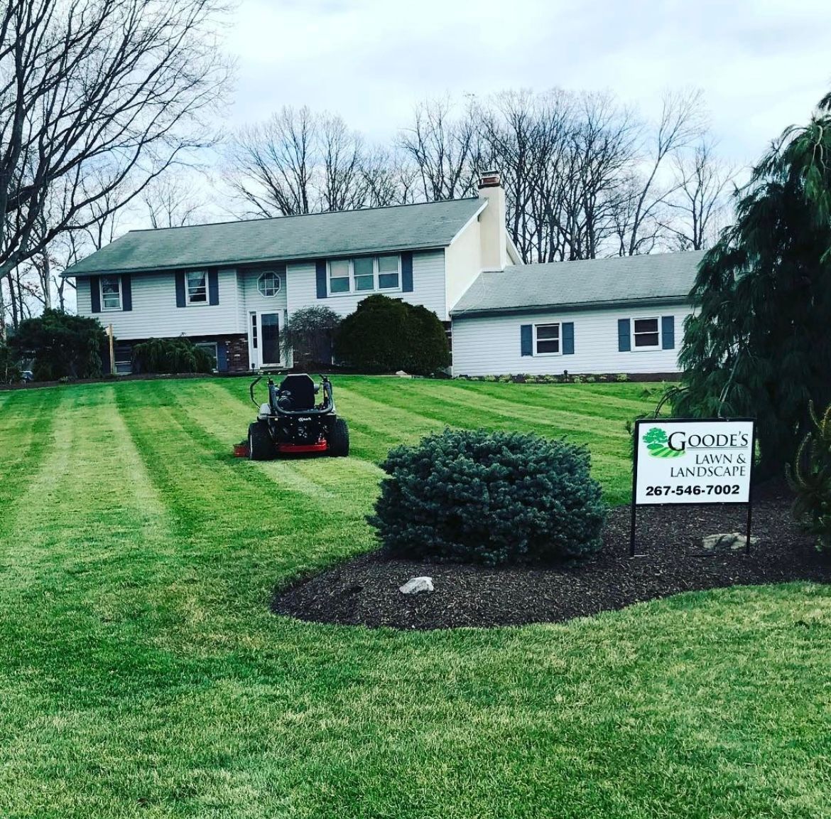A lawn mower is cutting a lush green lawn in front of a house.