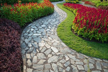 A stone walkway in a garden surrounded by flowers and grass.