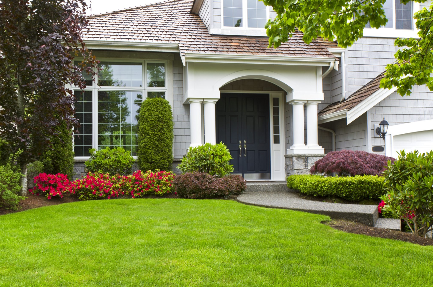 A large house with a lush green lawn and flowers in front of it.