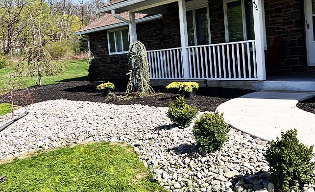 A brick house with a porch and a rock garden in front of it.
