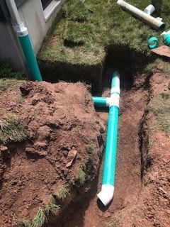 A green pipe is being installed in a hole in the ground.