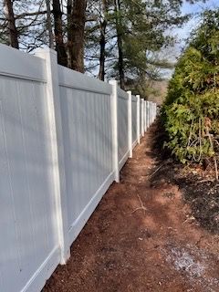 A white vinyl fence along a dirt path surrounded by trees.