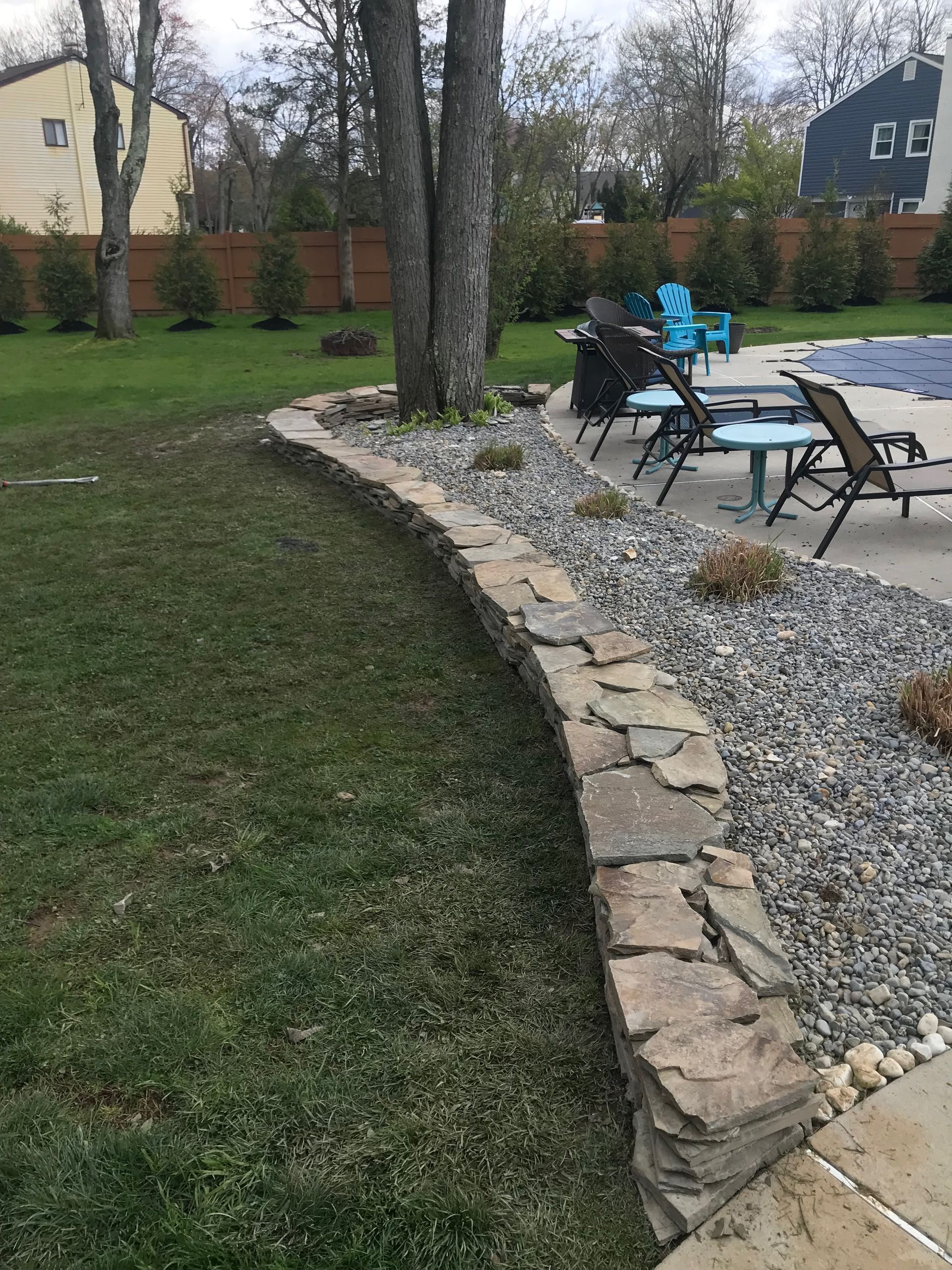 A stone wall surrounds a patio area with chairs and a table.