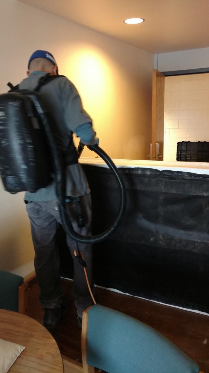 A man with a backpack is using a vacuum cleaner.