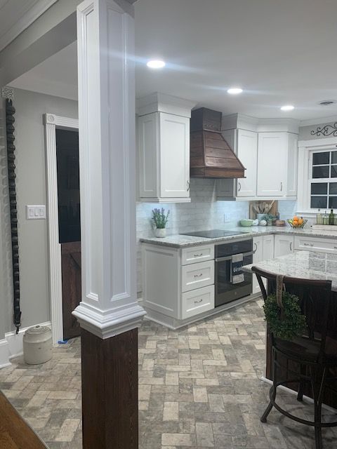 A kitchen with white cabinets , a stove , a table and chairs.