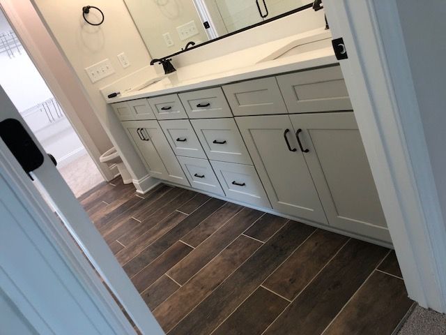 A bathroom with white cabinets and brown tile floors