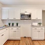 A kitchen with white cabinets , hardwood floors , a microwave , and a sink.