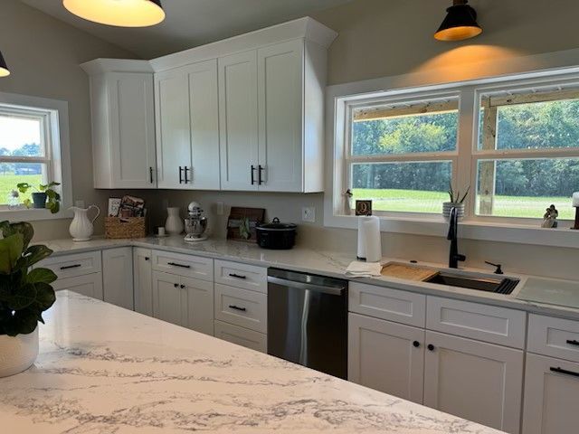 A kitchen with white cabinets , a sink , a dishwasher , and two windows.